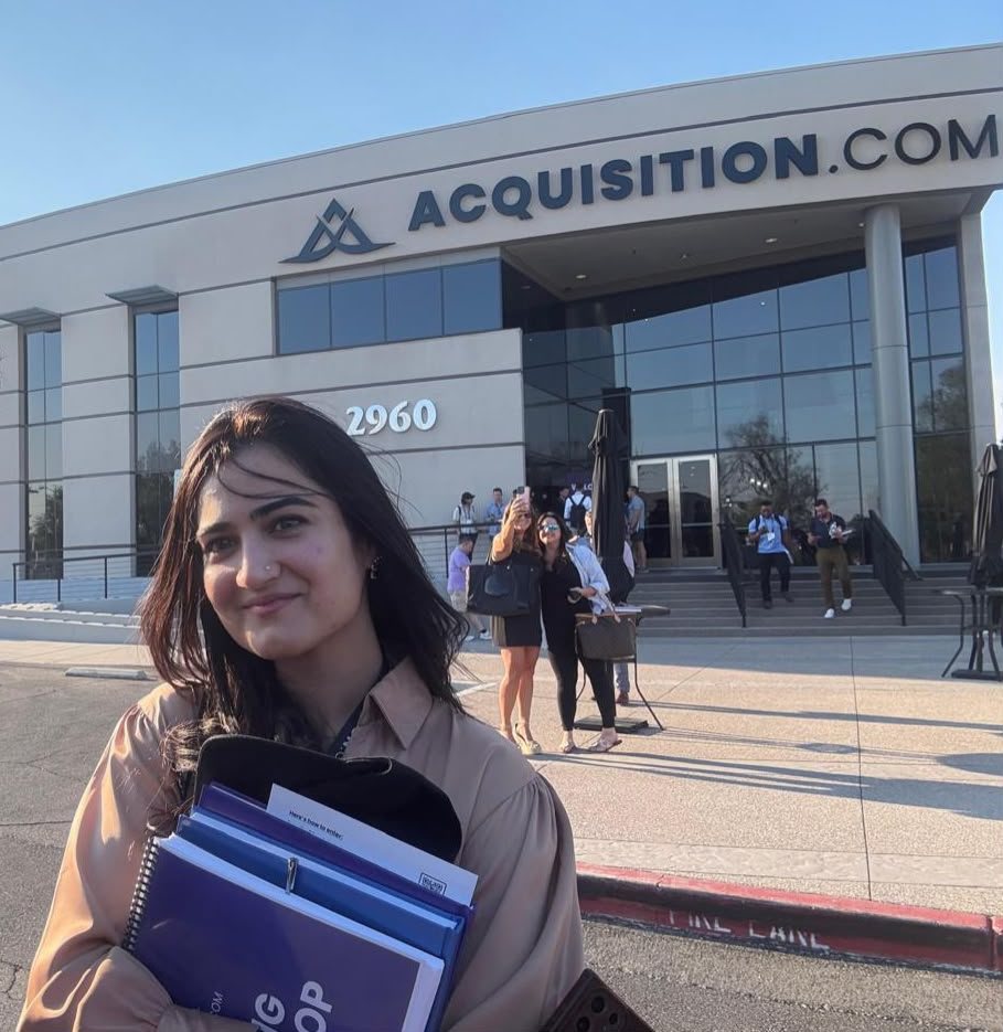 Sana outside Acquisition.com headquarters holding workshop binders